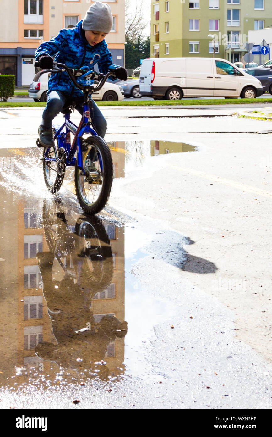 Jungen Kind mit dem Fahrrad auf der anderen Seite der Pfütze in der Straße, Sopron, Ungarn Stockfoto