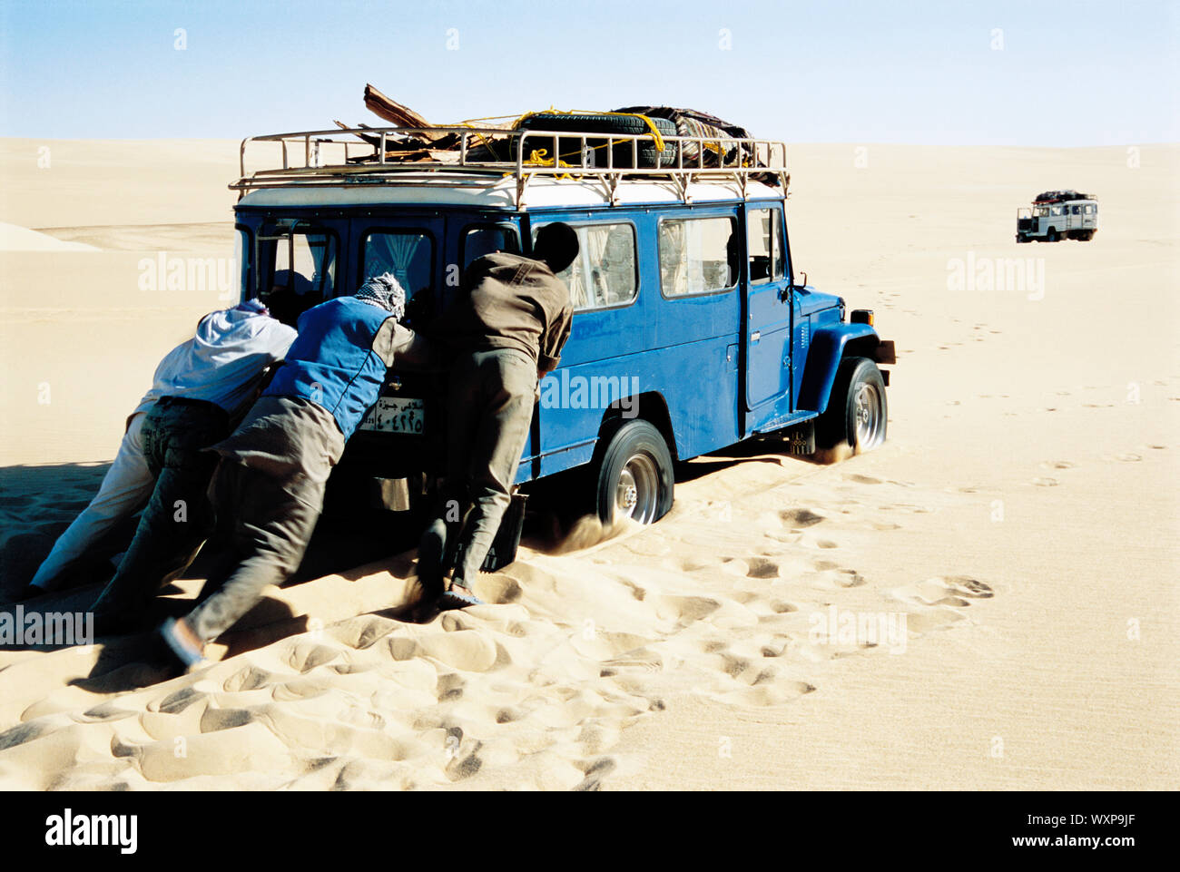 Männer schieben Jeep in die Wüste Stockfoto