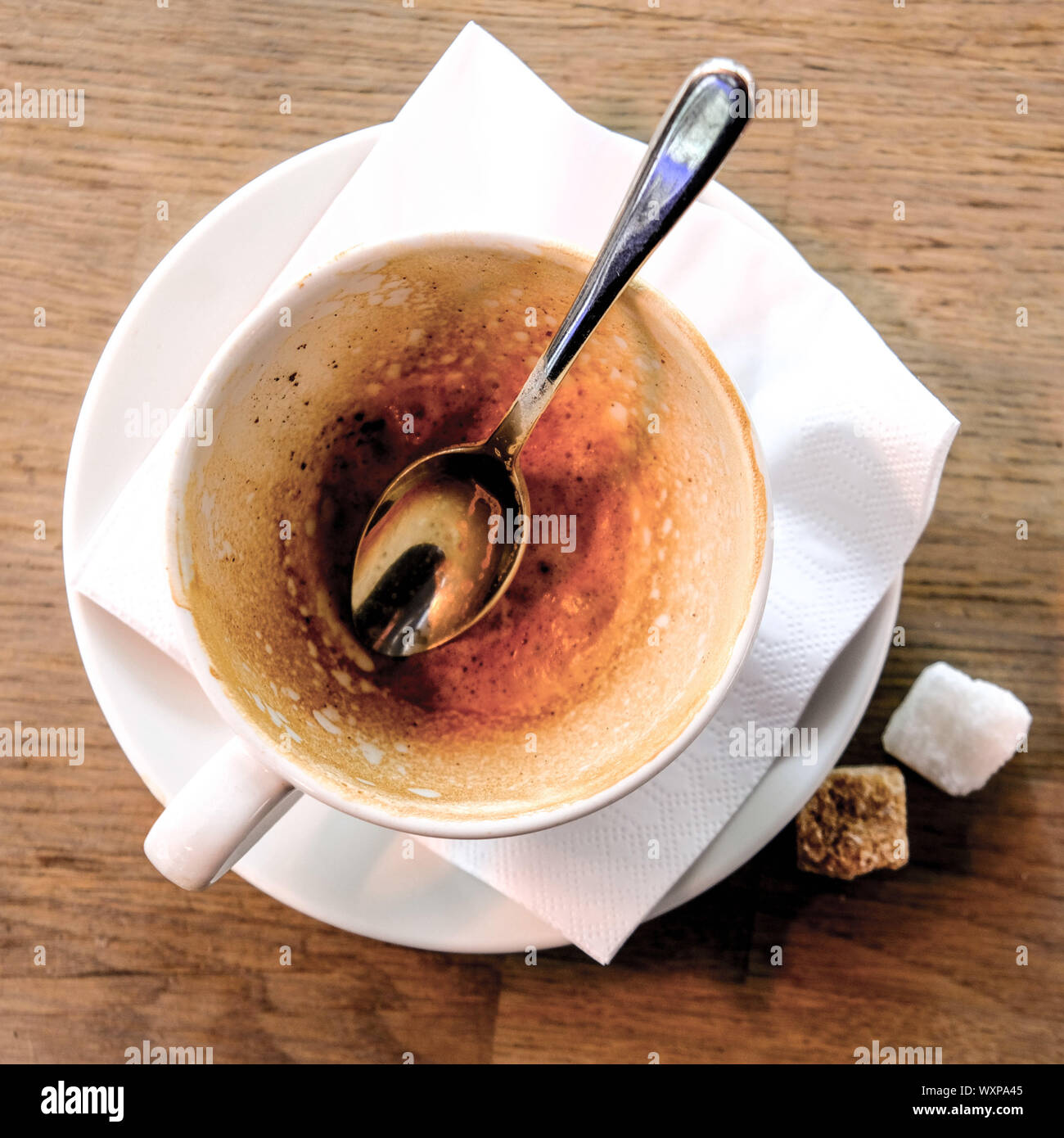 Auf der Suche nach einem leeren verwendet Tasse Cappuccino mit einem Löffel und Zwei von Würfelzucker auf einem Tisch Stockfoto
