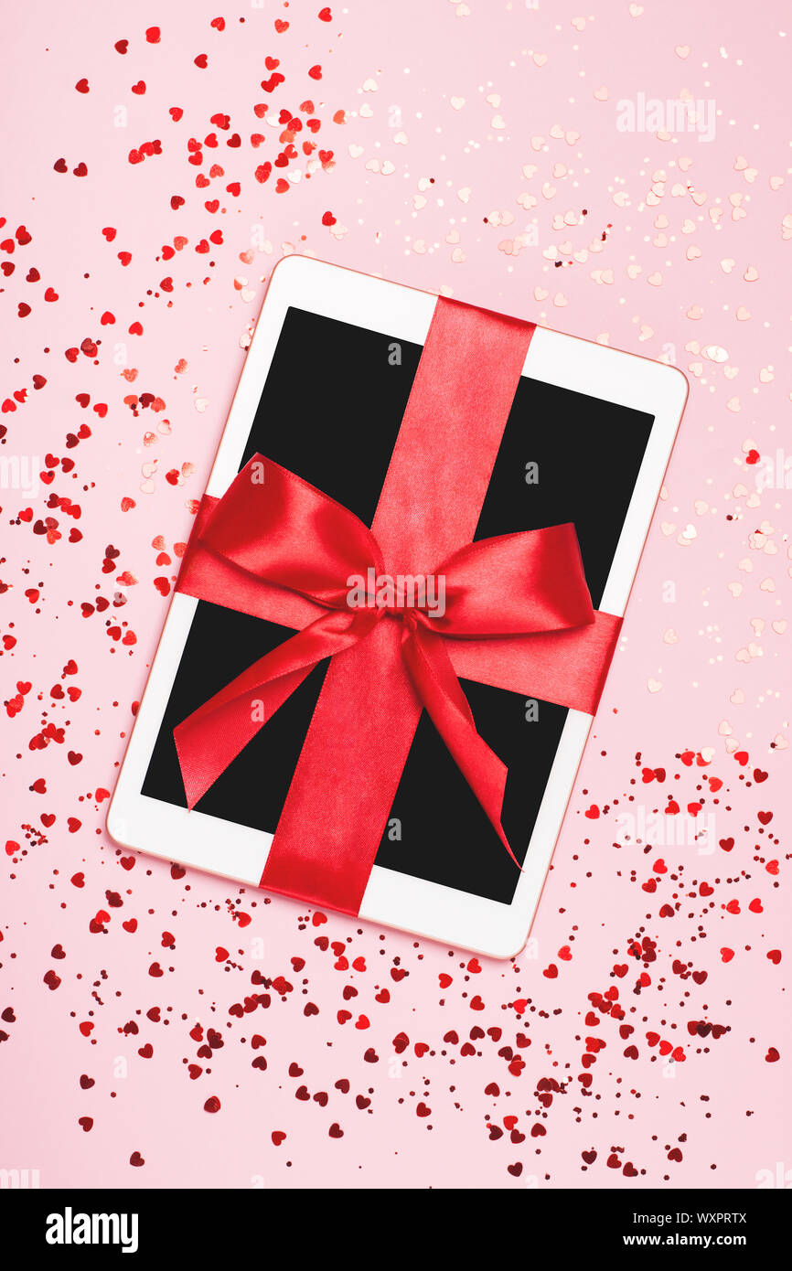 Die Tablette verpackt als Geschenk für Ihre Liebsten. Luxus roten Bogen und Pink sparkles Hintergrund. Das Konzept der Tag des St. Valentin, Liebe, Überraschungen. Flach Stockfoto