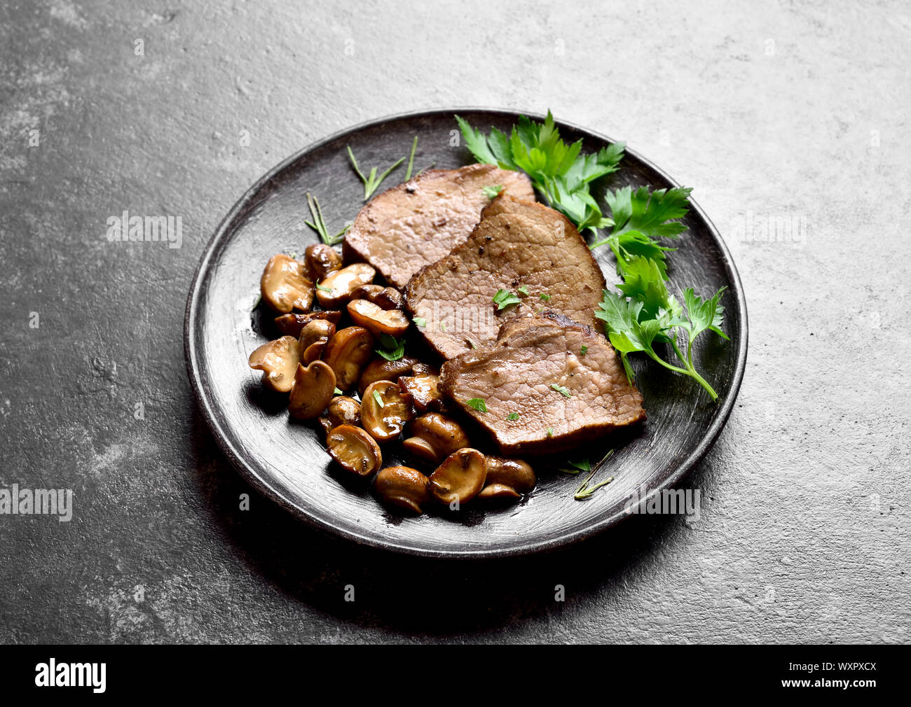 Langsam gekochtes Rindfleisch mit Pilzen auf dunklem Stein Hintergrund. Leckeren Fleischeintopf mit Pilzen. Nähe zu sehen. Stockfoto