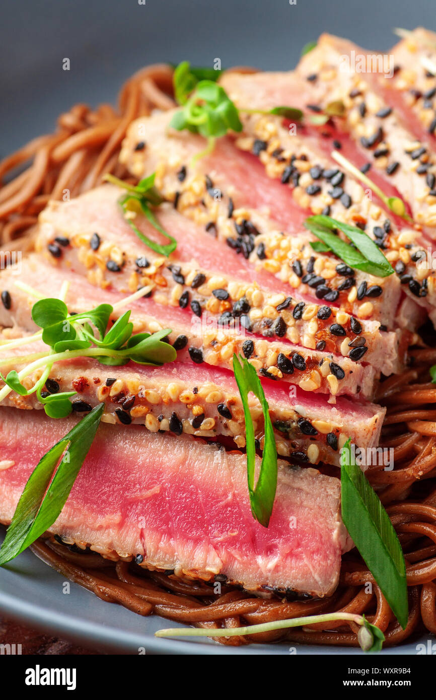 Japanische Soba-Nudeln Buchweizen mit in Scheiben geschnittenen Thunfisch mit Sesam auf dunklen Holztisch Stockfoto