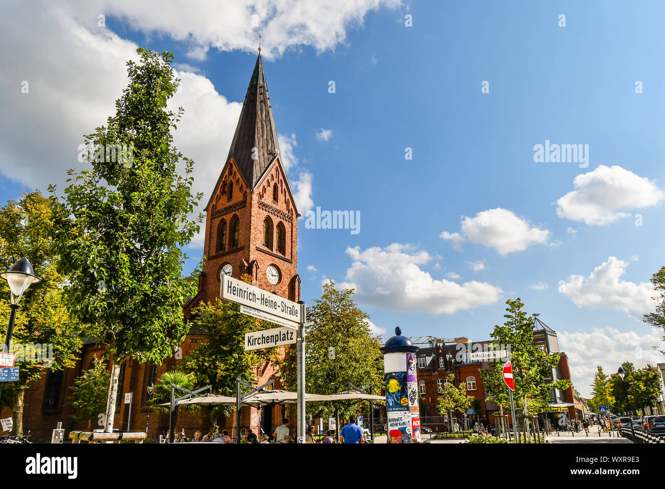 Die neo-gotischen Warnemünder Kirche Turm erhebt sich über die Altstadt von Rostock, Deutschland, als Touristen und Deutsche speisen Sie auf der Terrasse im Freien Platz. Stockfoto