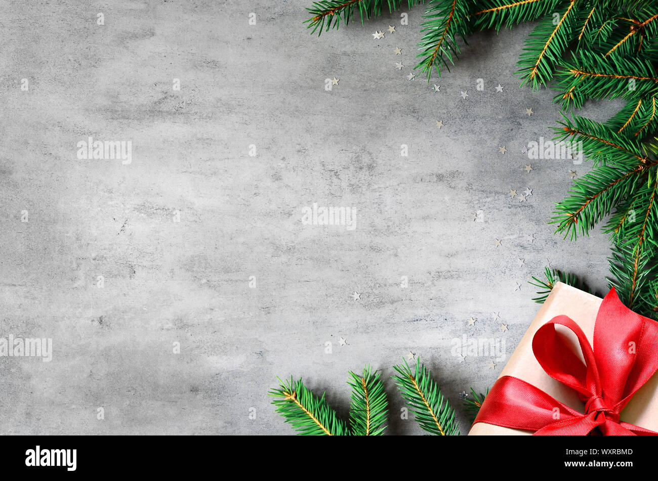 Weihnachtsgeschenke mit roter Schleife auf grauem Hintergrund in einem Rahmen aus Tannenzweigen. Flach, Ansicht von oben. Weihnachten Hintergrund. Stockfoto