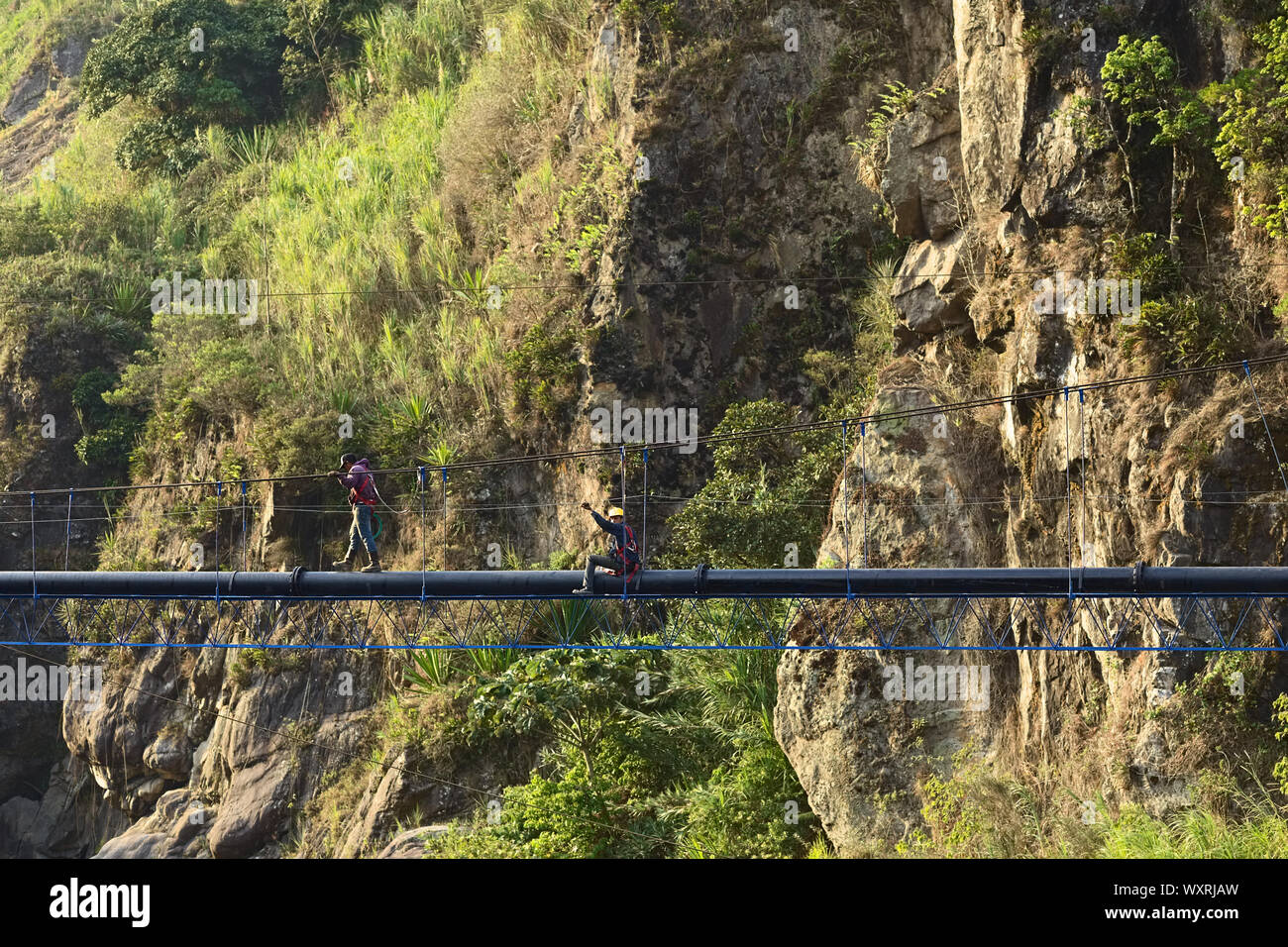 BANOS, ECUADOR - 18. FEBRUAR 2014: Unbekannte junge Männer arbeiten an einer Rohrleitung über dem Canyon des Flusses Pastaza in Banos, Ecuador Stockfoto