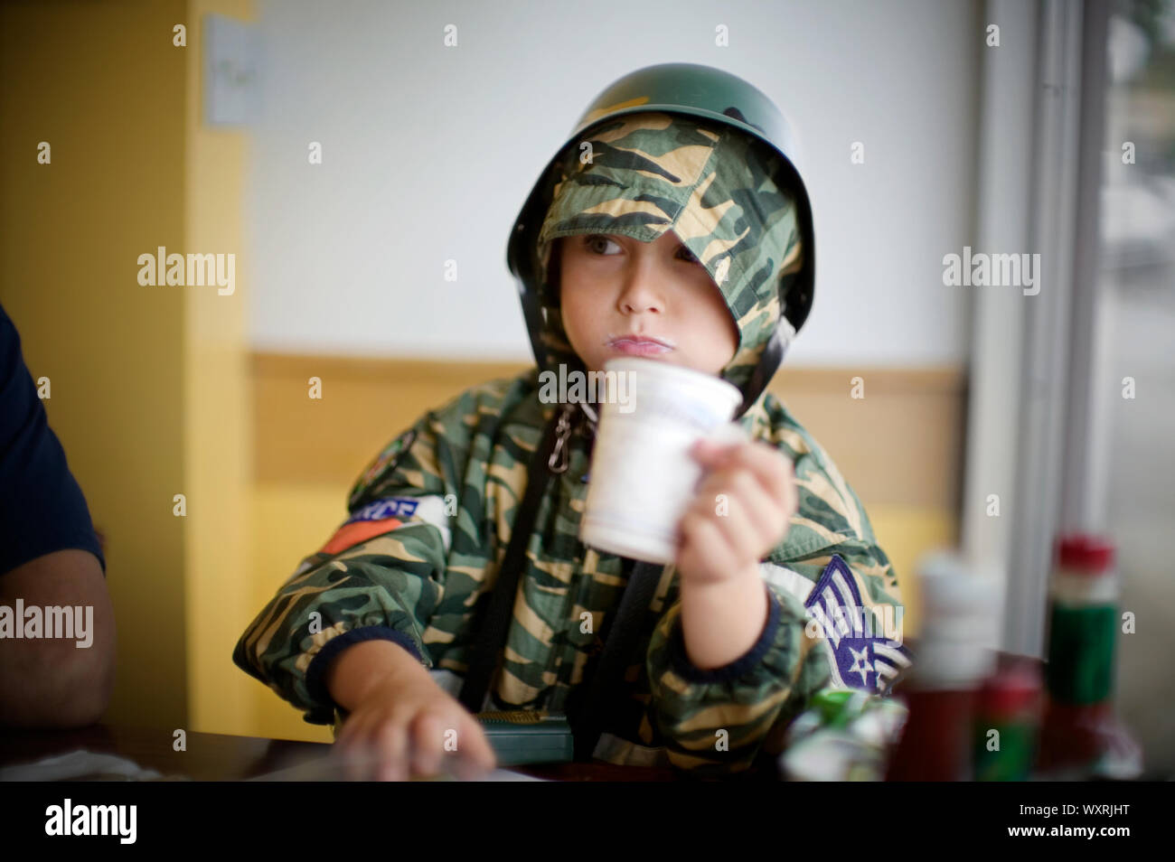 Junge Holding eine Tasse, während das Tragen eines Helmes und Camouflage Kleidung. Stockfoto