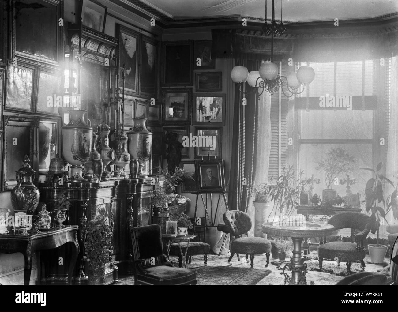AJAXNETPHOTO. 1922. AGRA, Indien. - Koloniales Interieur - WOHNZIMMER EINES KOLONIALEN RESIDENCE GEFÜLLT MIT ARTEFAKTEN, darunter Gemälde, Schmuck, kurzes Bein Stühle, Tische und Topfpflanzen. Foto: T.J. SPOONER COLL/AJAX VINTAGE BILDARCHIV REF; 1922 104 Stockfoto