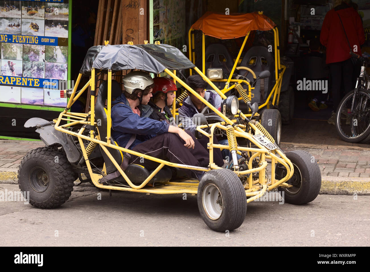 BANOS, ECUADOR - 25. FEBRUAR 2014: Unbekannte Personen in einem Buggy vor einem Reiseveranstalter und Fahrzeugvermietung in der Straße 16 de Diciembre in Banos Stockfoto