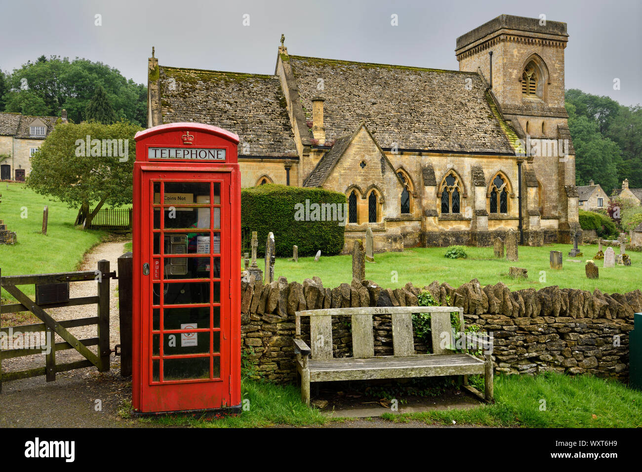 Rote Telefonzelle an mittelalterliche St. Barnabas anglikanische Kirche mit Friedhof und Mauer Tor in feuchten regnerischen Wetter in Snowshill Cotswold England Stockfoto