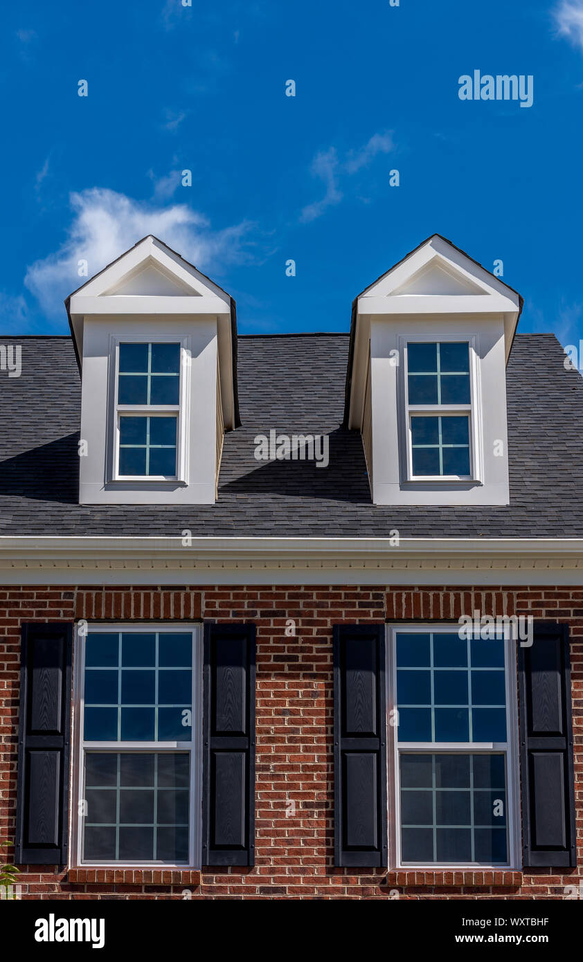 Dachfenster mit doppelte Fenster shutter Windows und Backsteinfassade auf ein Einfamilienhaus mit blauem Himmel Stockfoto