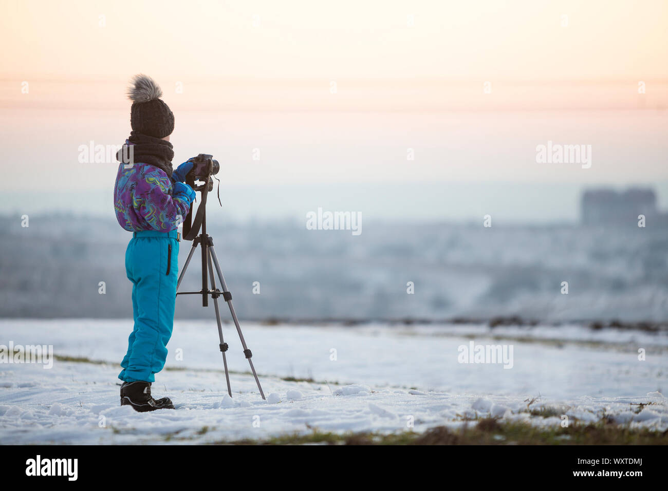 Kind Junge Fotografieren im Winter draußen mit Foto Kamera auf einem Stativ auf schneebedeckten Feld. Stockfoto