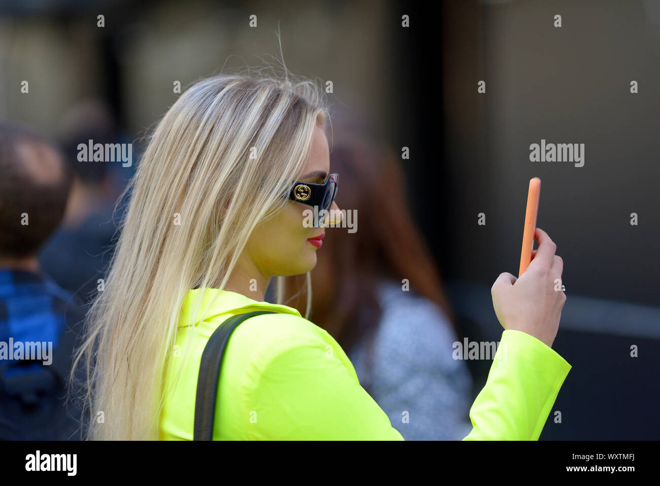 Junge Frau in hellem Gelb mit Orange Handy bei der London Fashion Week, 2019. Stockfoto