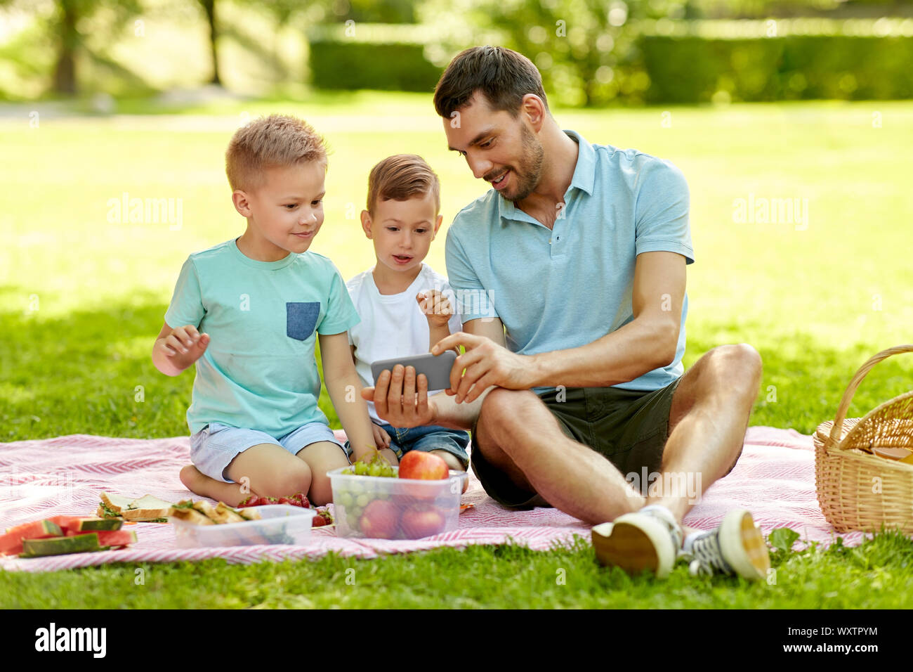 Familie, Freizeit und Personen Konzept - glücklicher Vater und zwei kleinen Söhnen mit Smartphone mit Picknick im Sommer Park Stockfoto