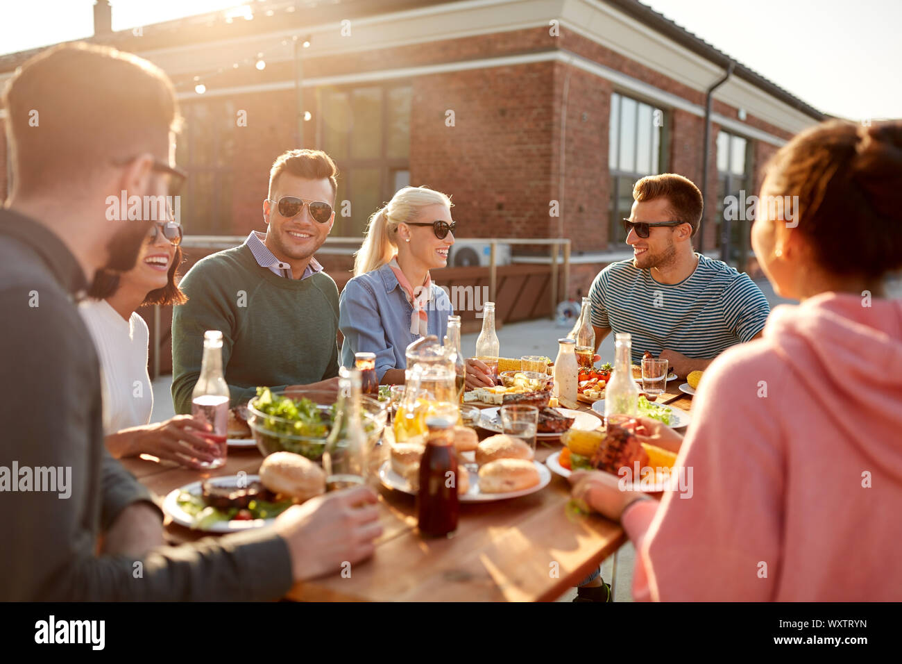 Freizeitaktivitäten und Personen Konzept - glückliche Freunde Abendessen oder Grillabend auf der Dachterrasse im Sommer Stockfoto