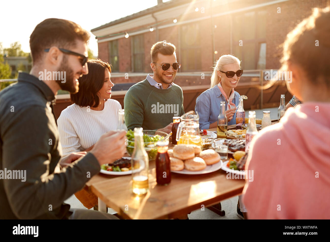 Freizeitaktivitäten und Personen Konzept - glückliche Freunde essen oder Grillen und Essen auf der Dachterrasse im Sommer Stockfoto