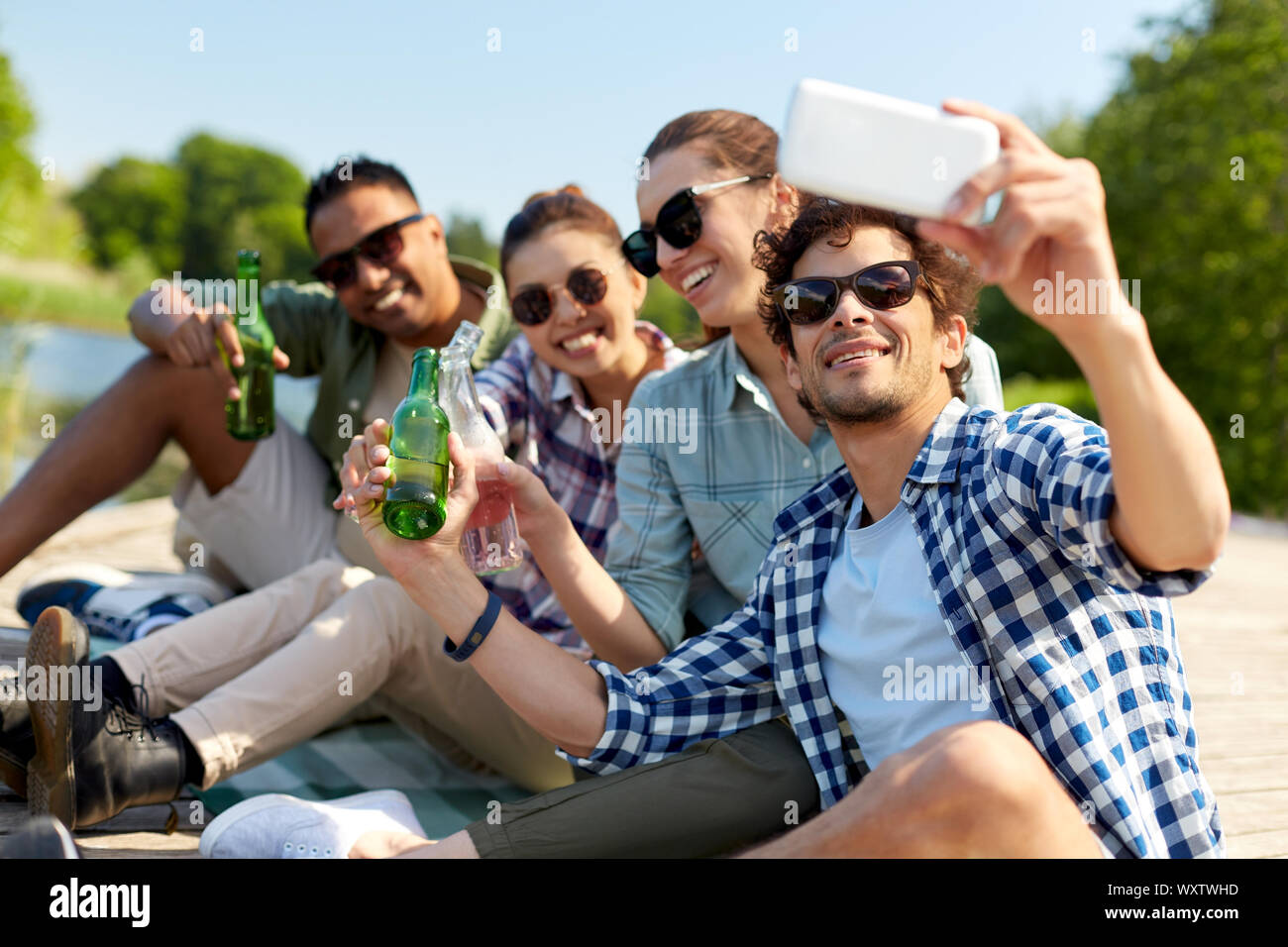 Freizeit-, Picknick- und Technologiekonzept - Freunde mit Getränken unter Berücksichtigung von selfie Smartphone auf See Pier im Sommer Park Stockfoto