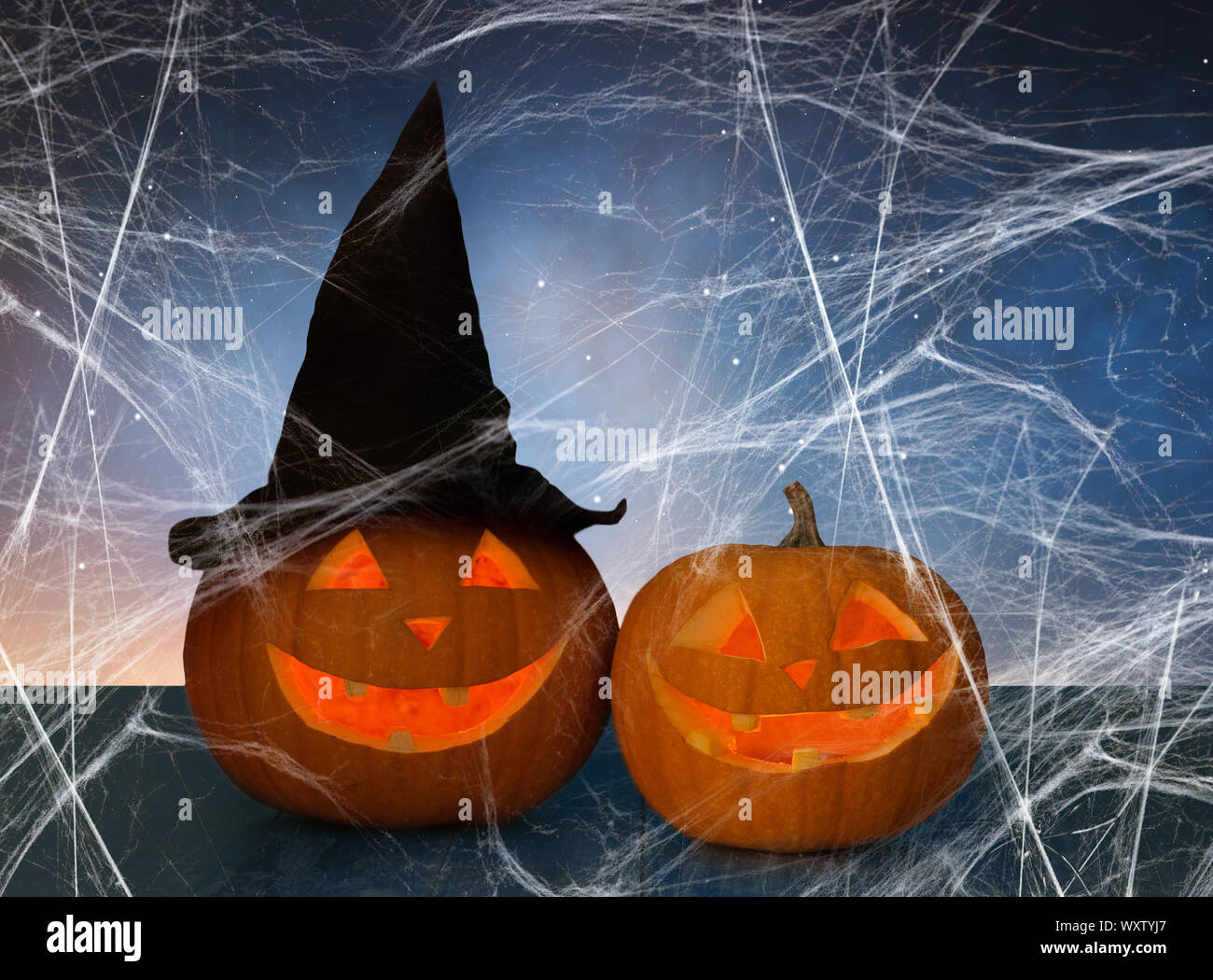 Urlaub, Halloween und die Dekoration - zwei kürbisse oder jack o Laternen in Hexe Hut auf dem Tisch und Spiderweb über Sternenhimmel Hintergrund Stockfoto