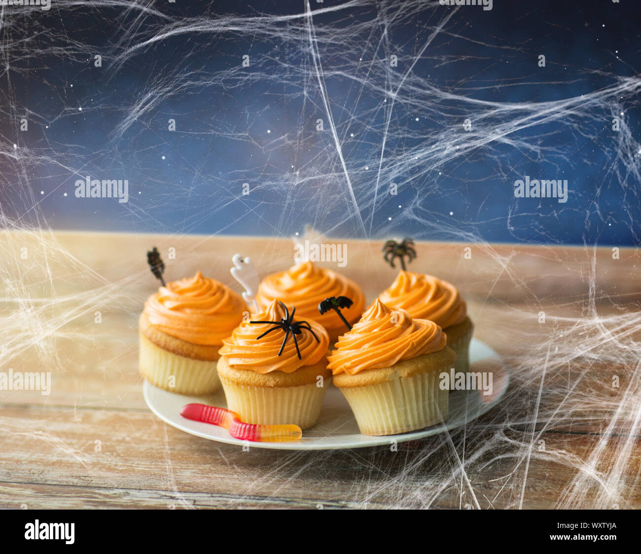 Essen, Backen und Urlaub Konzept - kleine Kuchen oder Muffins mit halloween party Dekorationen, Jelly Wurm Candy und Spiderweb auf hölzernen Tisch über starry n Stockfoto