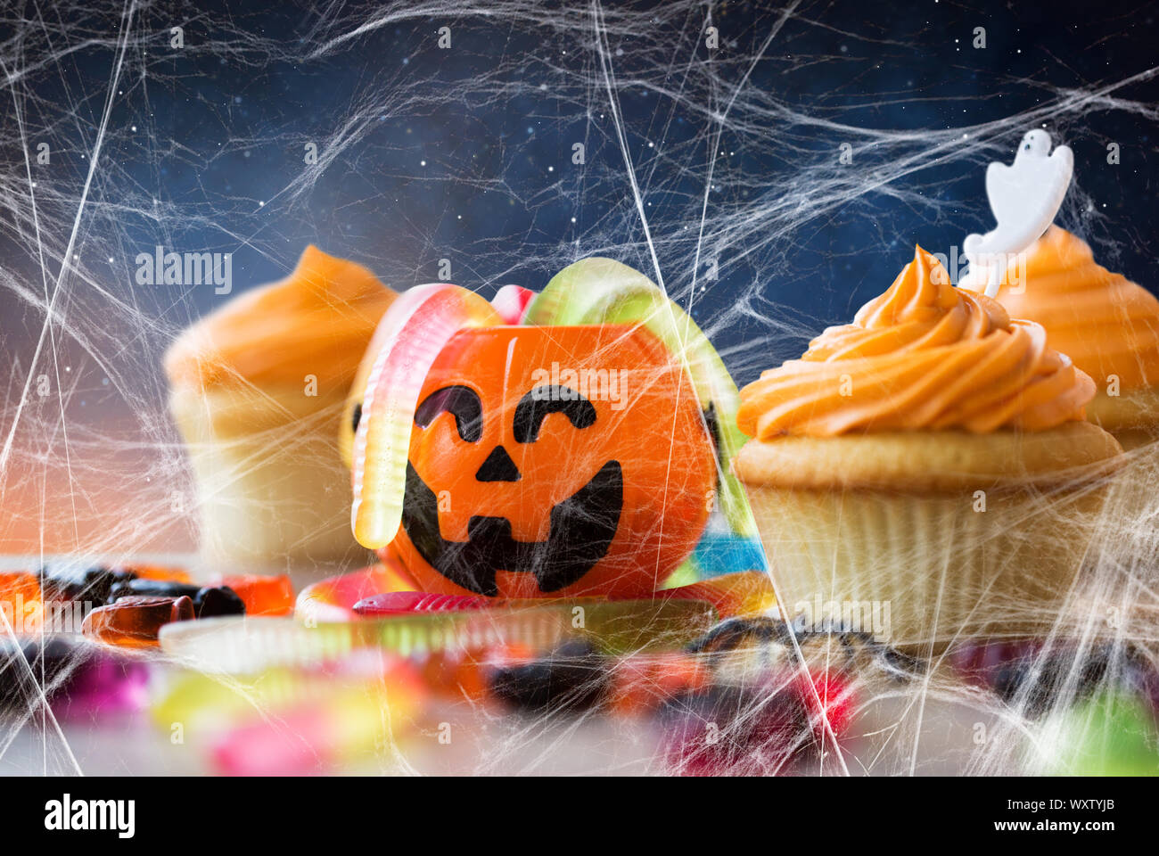 Essen, Backen und Urlaub Konzept - kleine Kuchen oder Muffins mit halloween party Dekorationen, Jack-o-Lantern, Jelly Wurm Bonbons und Spiderweb auf Holz- t Stockfoto