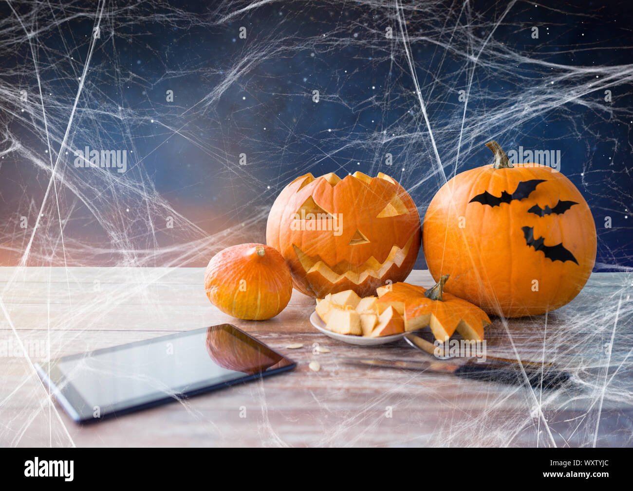 Urlaub, Halloween und Technologie Konzept - Jack-o-Lantern oder geschnitzten Kürbis, tablet pc, Messer auf Holztisch und Spiderweb über starry nig Stockfoto