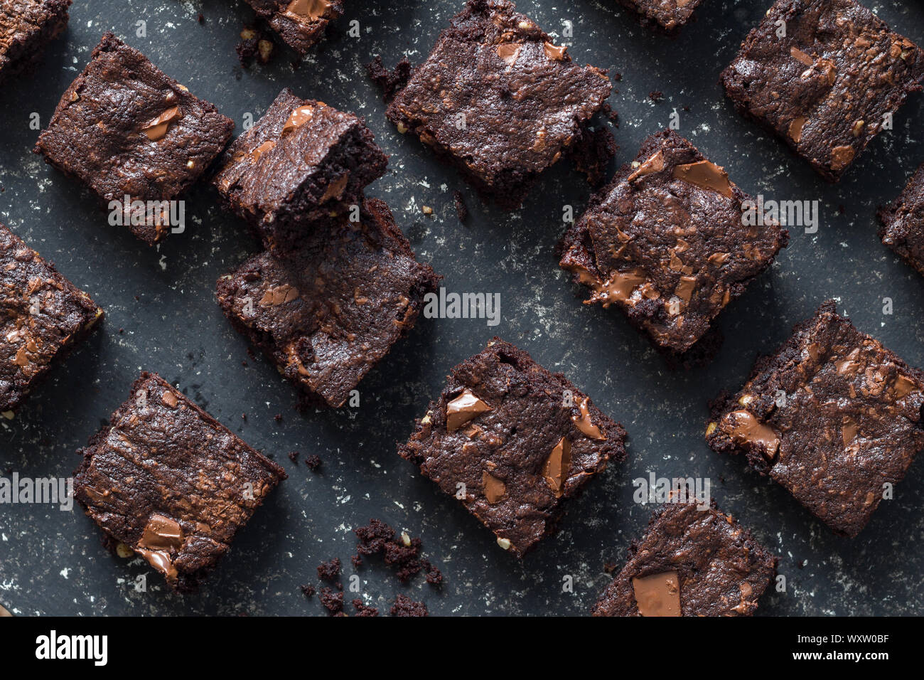 Gebackene Chocolate Brownie Quadrate auf meliert grau Hintergrund Textur - Blick von oben auf die Brownies mit geschmolzener Schokolade Bits Stockfoto
