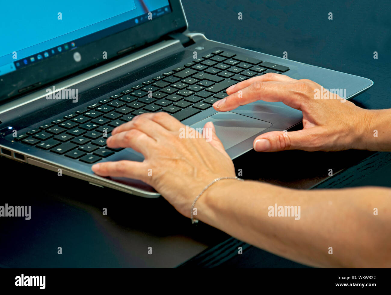 Eine Nahaufnahme eines womans Hände schreiben auf einen Laptop Tastatur auf einem schwarzen Schreibtisch. Stockfoto