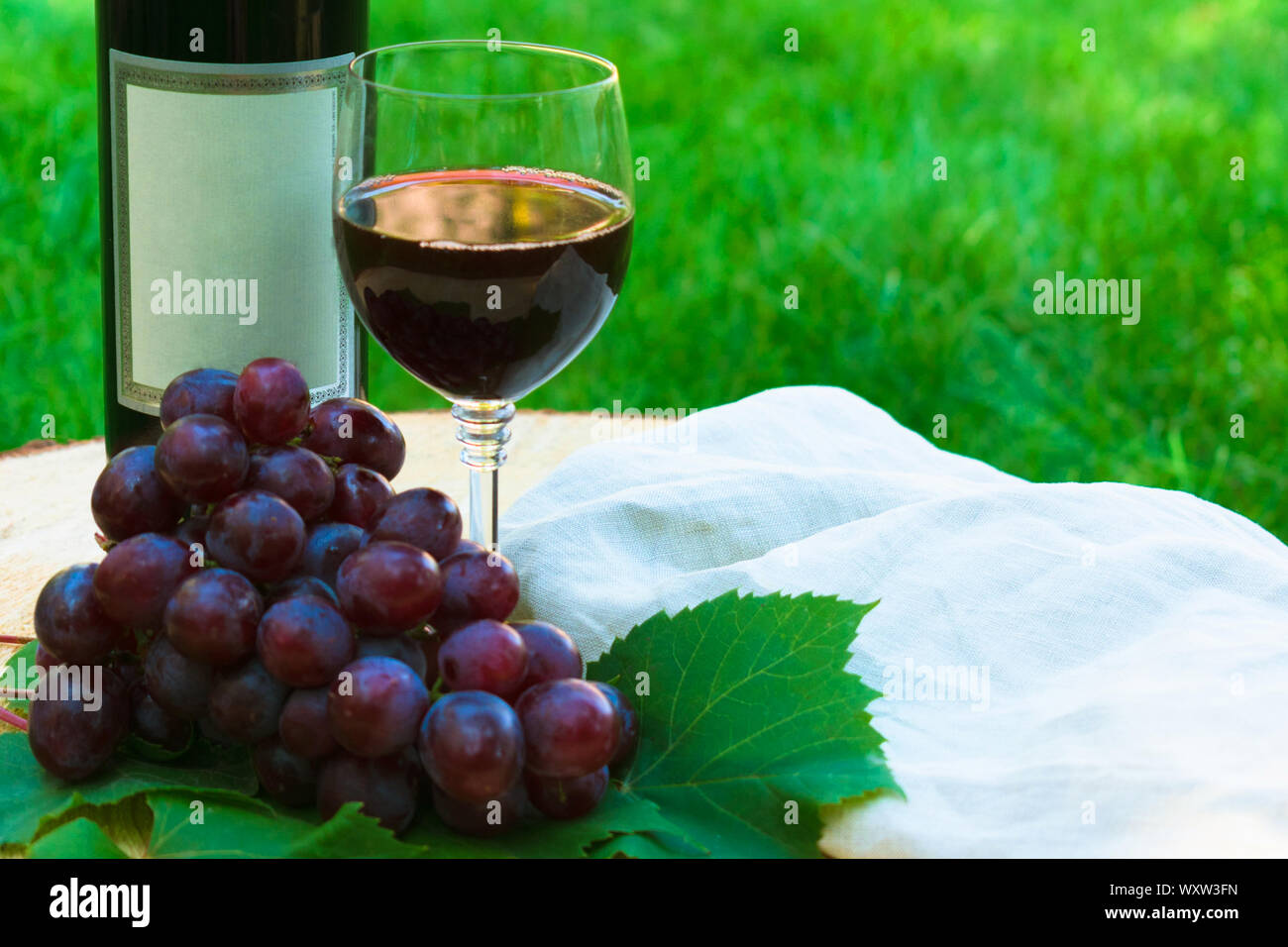 Rotwein in ein Glas und ein Bündel von vinograda auf einem Holztisch vor dem hintergrund der grünen Gras. Close-up. Stockfoto