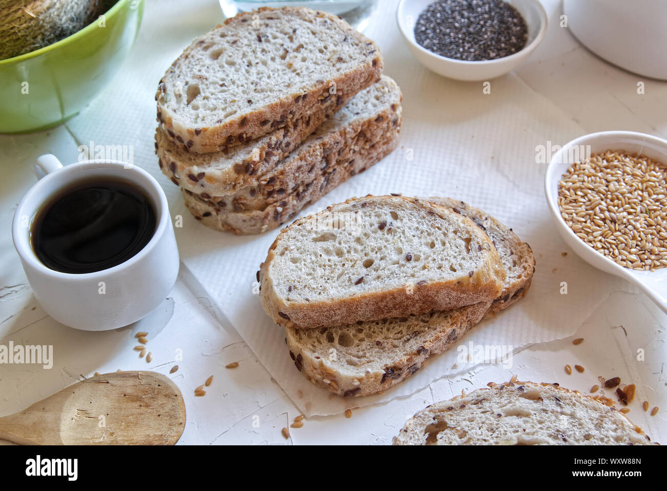 Braun Brot mit Getreide neben einer Tasse Kaffee auf einem weißen Tisch von einem rustikalen Küche. Samen und Zutaten für zu Hause Bäckerei. Stockfoto