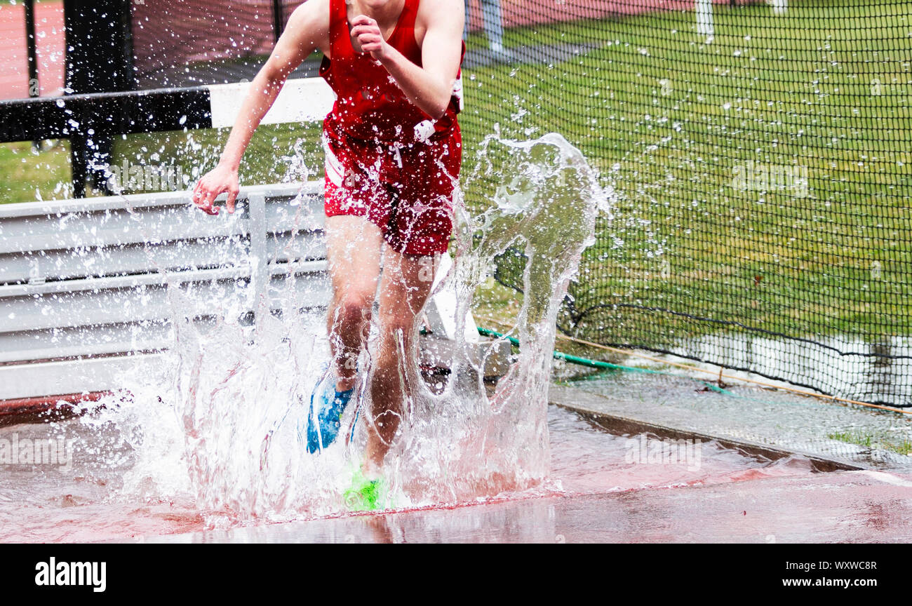 Ein High School boy Landung im Wasser während eines Steeplechase-cross und Spritzwasser überall. Stockfoto