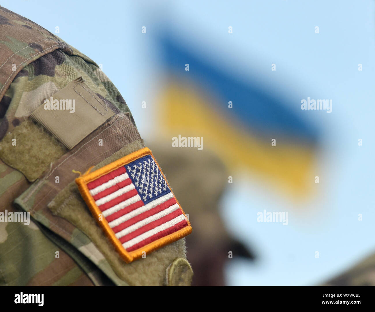 Amerikanische Flagge auf Soldaten arm und Flagge der Ukraine im Hintergrund. Uns militärische Hilfe an die Ukraine. Stockfoto