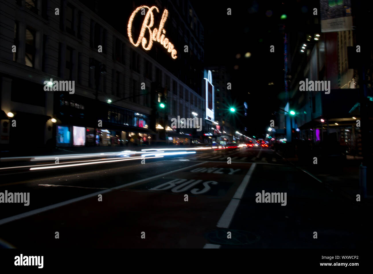 New York city street view in der Nacht als Autos vorbei und die Worte glauben leuchtet in einem Gebäude Stockfoto