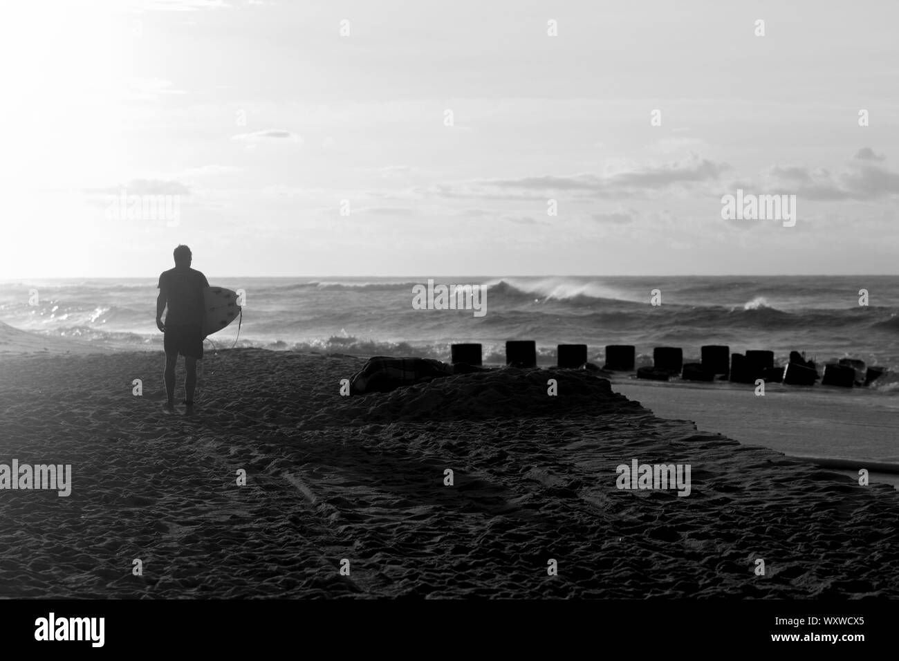 Ein schwarz-weiß Bild von einem Surfer, der Strand bei Sonnenaufgang, am Wasser suchen Stockfoto