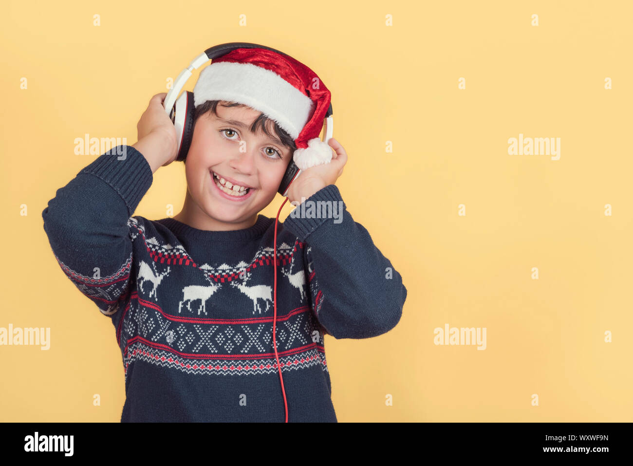 Glückliches Kind tragen Weihnachten Weihnachtsmann Mütze mit Kopfhörer auf gelbem Hintergrund Stockfoto