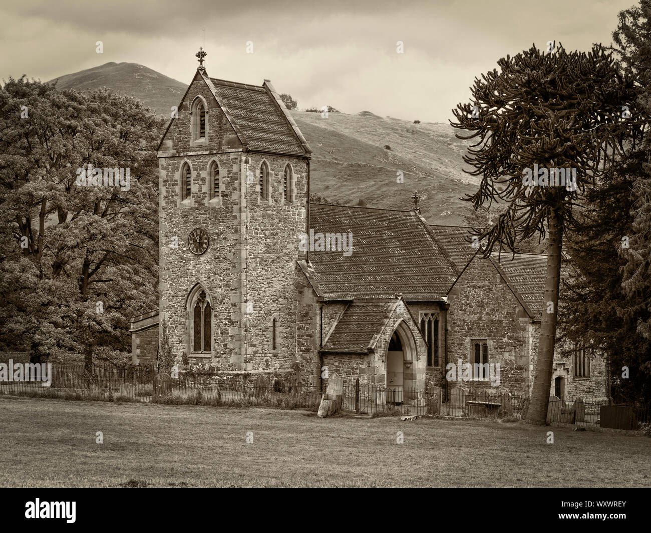 Die kleinen alten Kirche im Dorf Ilam, Staffordshire mit den Hügeln des Peak District National Park im Hintergrund. Sepia getonten Bild Stockfoto