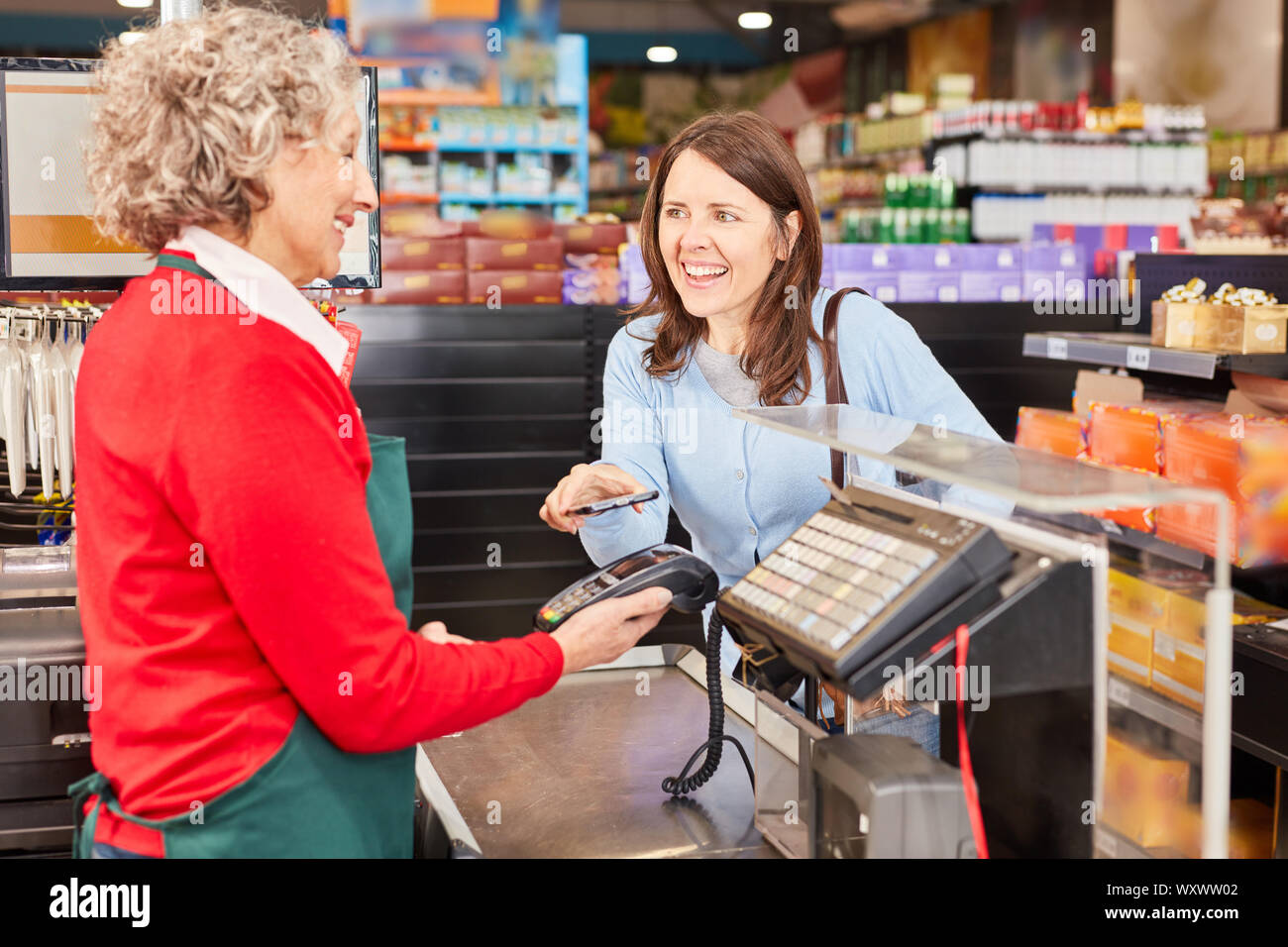 Junge Frau macht mobile Payment mit NFC-Smartphone an der Supermarktkasse Stockfoto