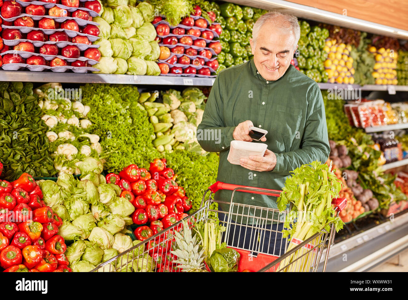 Älterer Mann mit Warenkorb und Smartphone während des Scannens, Essen Stockfoto