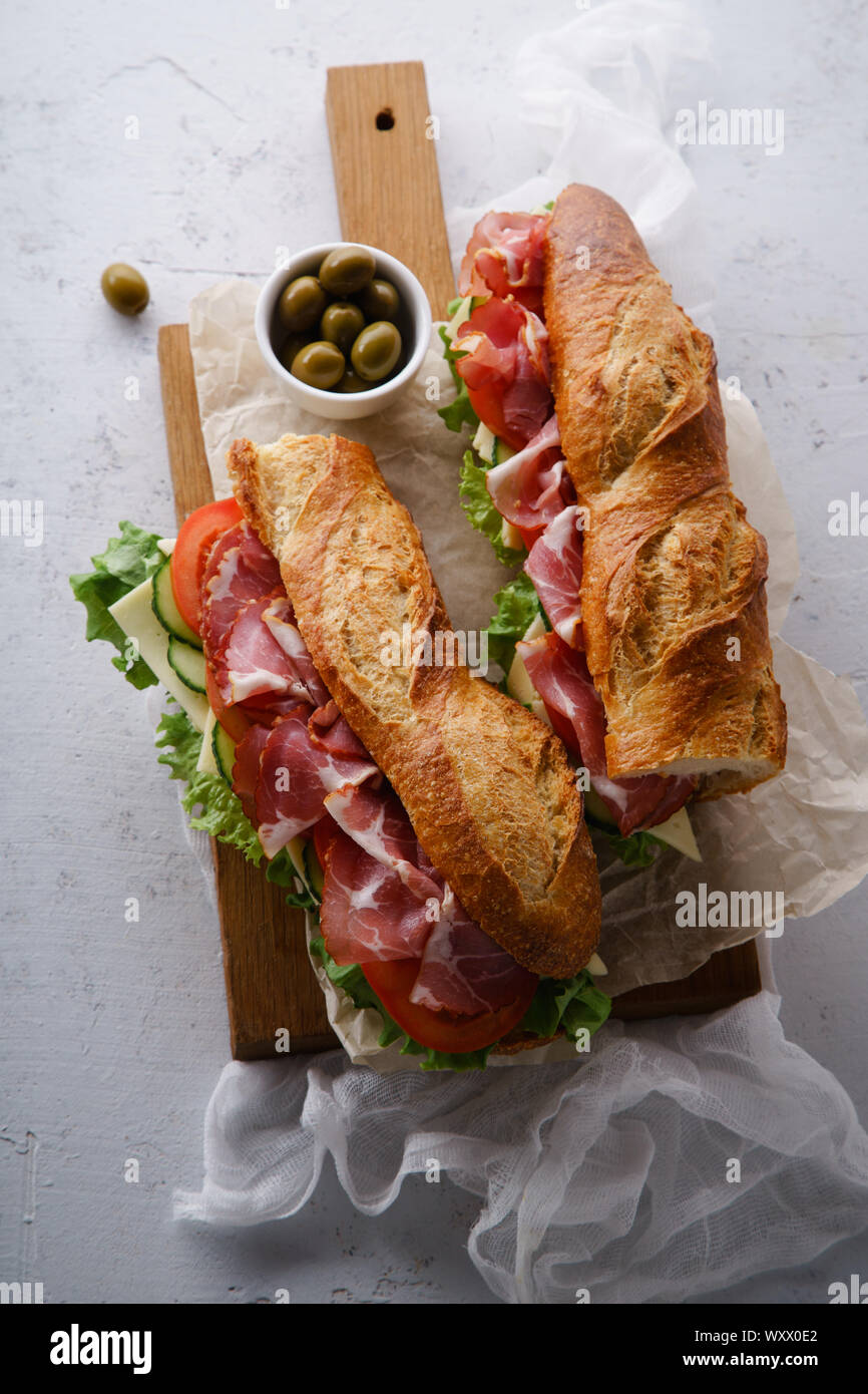 Blick von oben auf die beiden frisch belegte Brötchen bahn-mi gestaltet. Schinken, in Scheiben Käse, Tomaten und frischem Salat auf dunklem Holz Schneidebrett auf Beton zurück Stockfoto