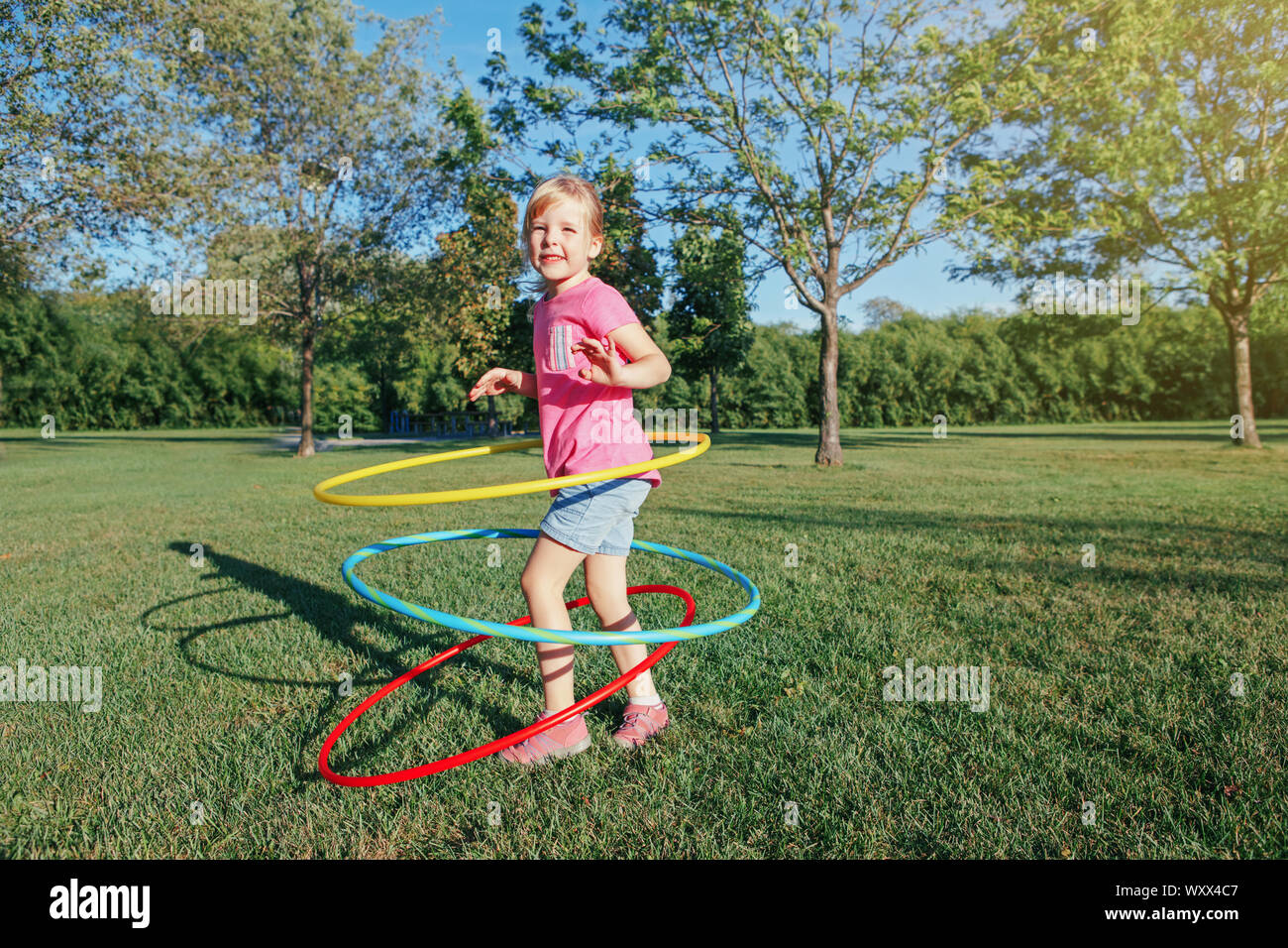 Nett Lächeln, Kaukasier Vorschule blonde Mädchen spielen mit hoola Hoop in Park draußen auf Sommertag. Kinder Sport. Lifestyle glücklich Stockfoto