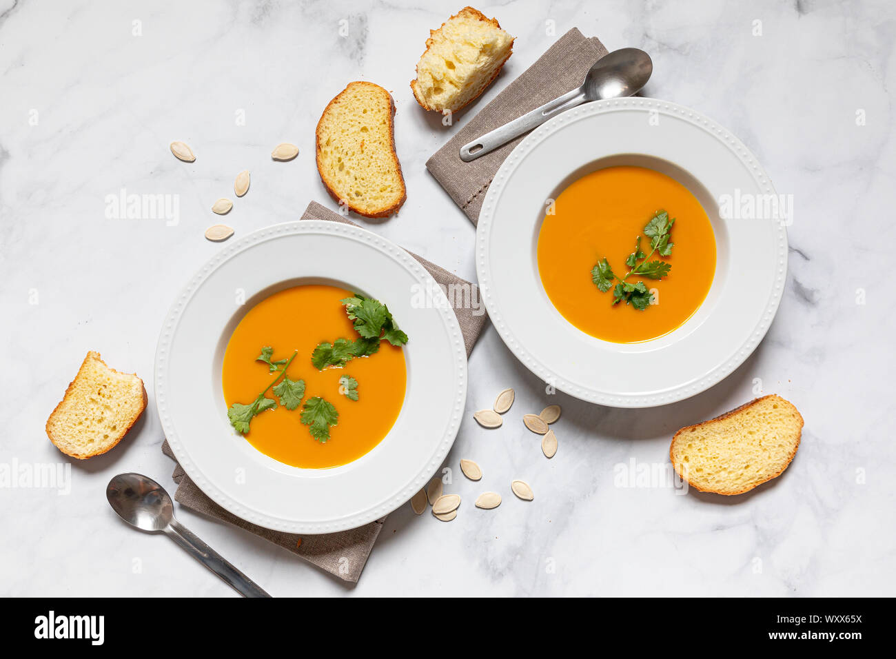 Pumpking Suppe serviert auf einem weißen Teller mit Brot und pumpking Samen von oben, flatlay Konzept gesehen Stockfoto