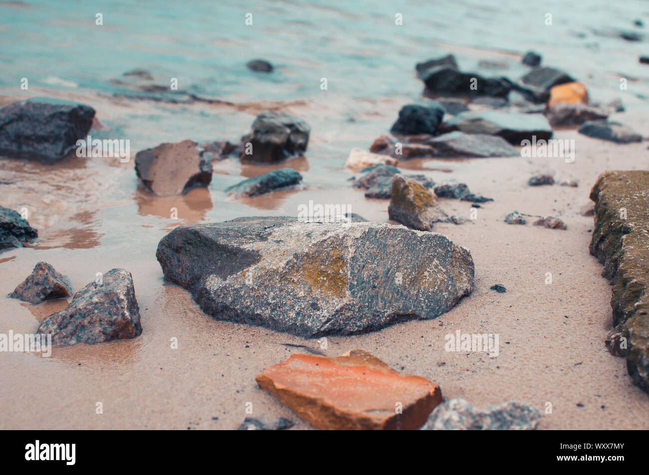 Kiesel auf einem sandigen Ufer in klares Wasser. Die seidigen Wellen eines blauen See schlug die Steine. Natürliche Hintergrund. Stockfoto