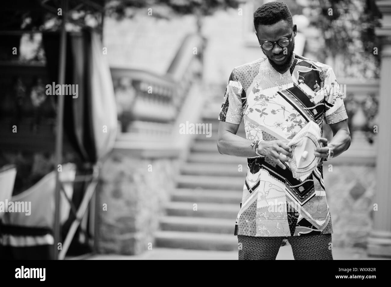 Stattliche afro-amerikanische Mann, der traditionellen Kleidung, Mütze und Brille in der modernen Stadt. Stockfoto