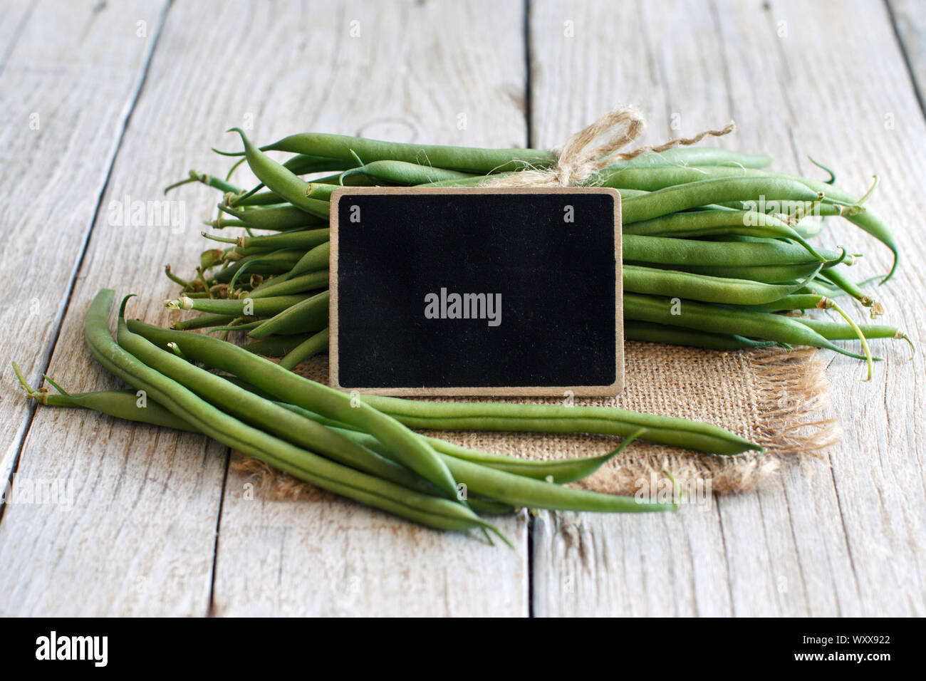 Frische grüne Bohnen mit einem kleinen schwarzen Brett auf einem hölzernen Hintergrund Stockfoto
