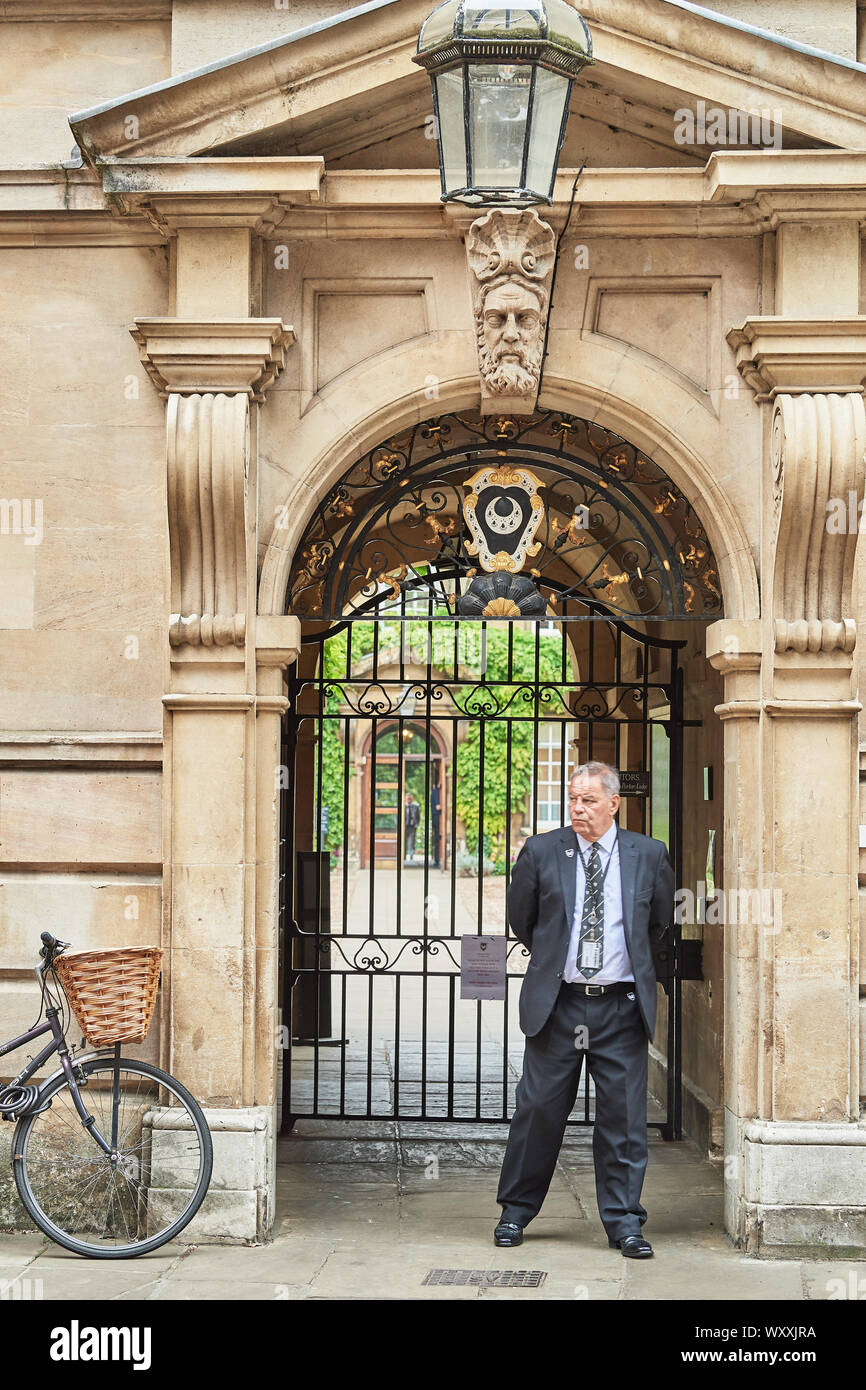 Ein männlicher Wachmann steht neben einem Zyklus vor dem Eingang zu Trinity Hall, Universität Cambridge, England, geparkt. Stockfoto