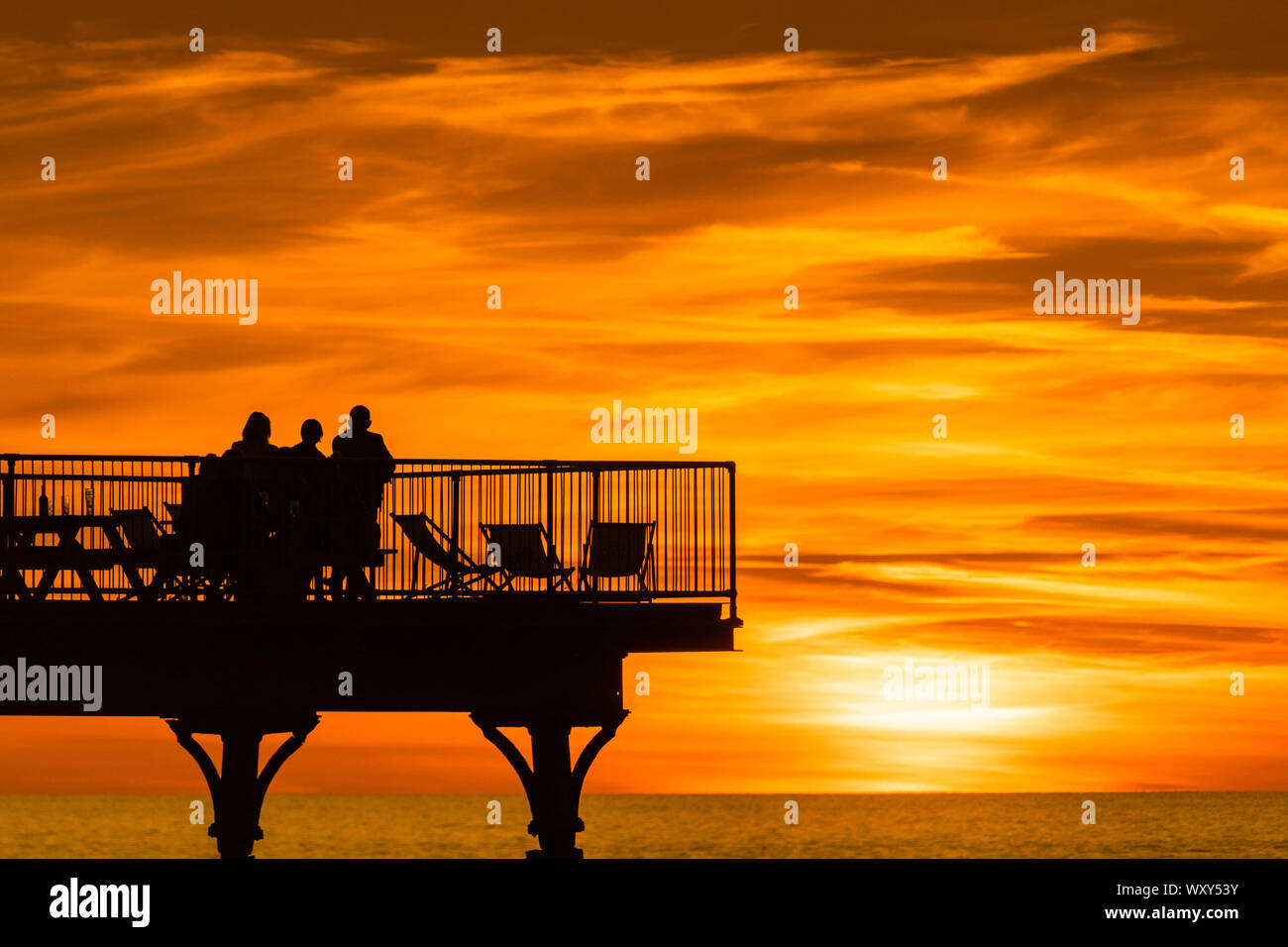 Aberystwyth, Großbritannien. 18 Sep, 2019. Aberystwyth Wales UK, Mittwoch, 18. September 2019 die Sonne herrlich über die Cardigan Bay Silhouetten Menschen am Meer Pier am Ende eines Tages des ungebrochenen klaren blauen Himmel und warmen September Sonnenschein in Aberystwyth, als die 'Indian Summer' mini Hitzewelle weiterhin über die südlichen Teile des UK Credit: Keith Morris/Alamy leben Nachrichten Stockfoto