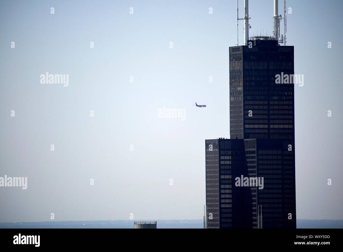 Ein Flugzeug fliegen vorbei an die Spitze der Willis Sears Tower mit Blick auf den Horizont, wie durch Glas aus dem Hancock Center Chicago Illinois gesehen un Stockfoto