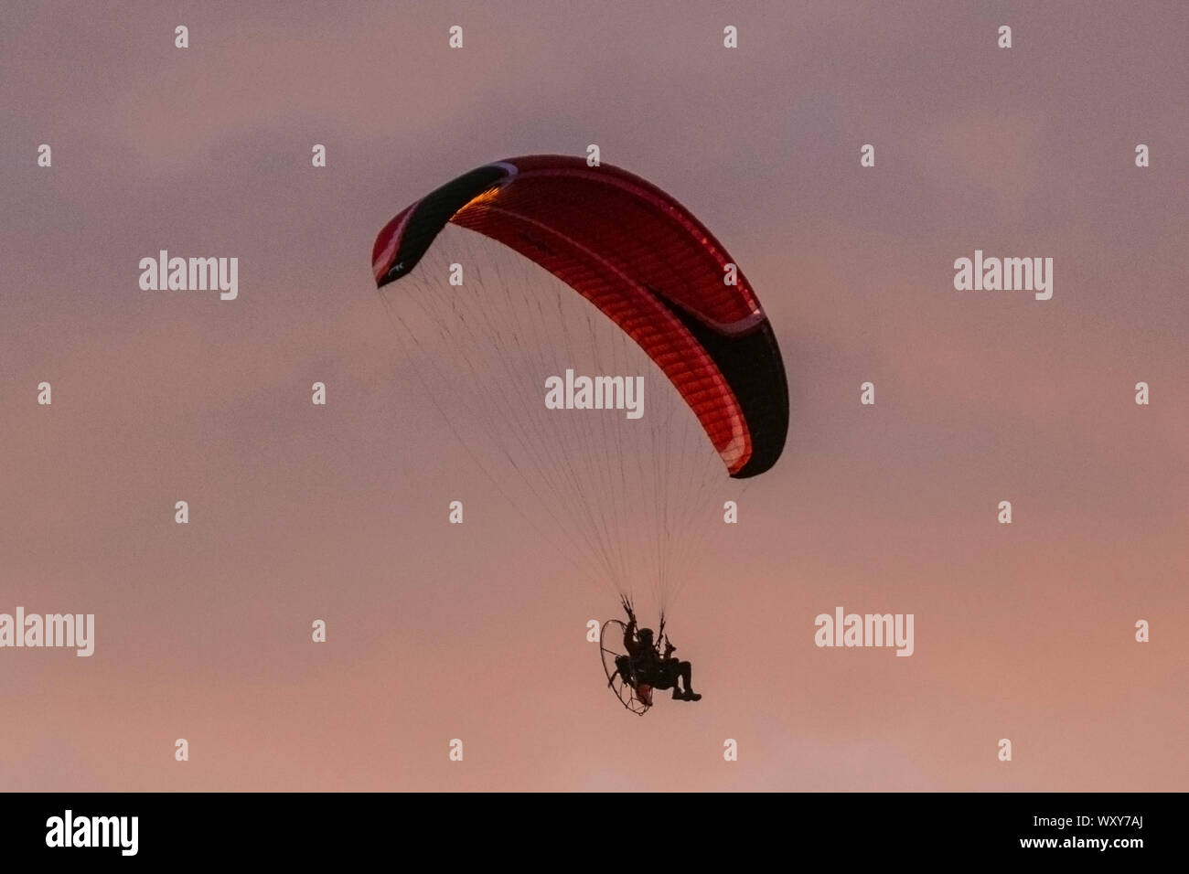 Ein motorbetriebener Handsegler, der in der Abendsonne geschildet wird, nimmt bei leichtem Wind einen motorisierten Flug, wenn die Sonne in Southport untergeht. Paramotor-Flugmaschinen & Stunt-Fliegen bei Sonnenuntergang; eine Handflieger-Silhouette vor orangen Wolken, die mit Propellermaschinen über der irischen Küste fliegen. Stockfoto