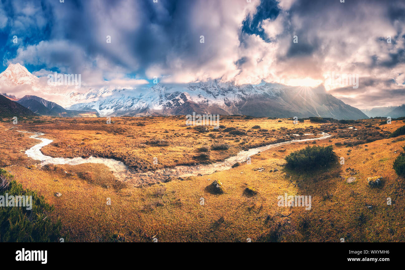 Berge mit schneebedeckten Gipfeln in lila Wolken und Fluss Stockfoto