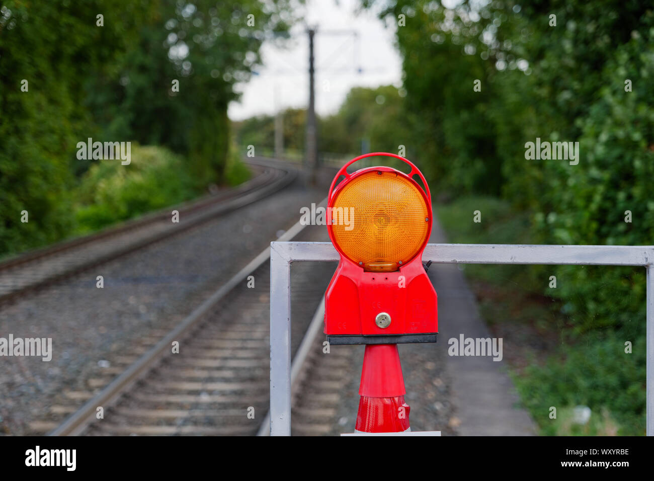 Nahaufnahme, blinkt und blinkt orange Achtung Licht am Ende der Plattform der Bahnhof über blur Hintergrund der Bahntrasse. Stockfoto