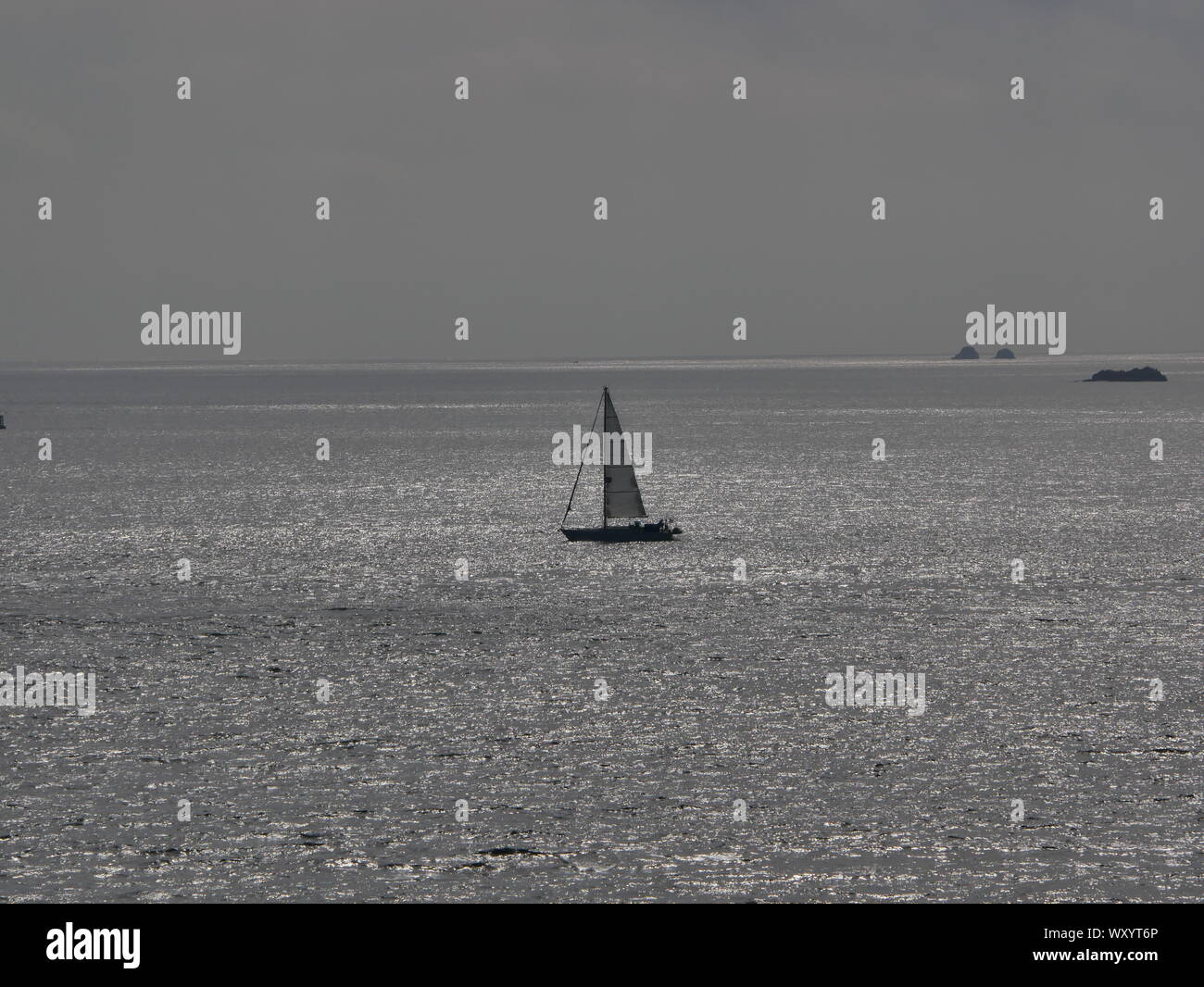 Foto de l'Océan a Contre Jour, avec un Voilier, océan Couleur argent a Contre Jour, îlots perdus en Mer Stockfoto
