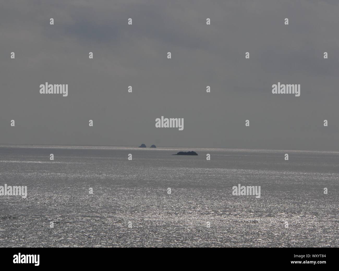 Foto de l'Océan a Contre Jour, avec un Voilier, océan Couleur argent a Contre Jour, îlots perdus en Mer Stockfoto